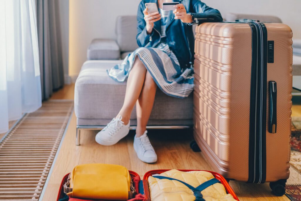 here is an image of a woman sitting with a suitcase booking a trip online