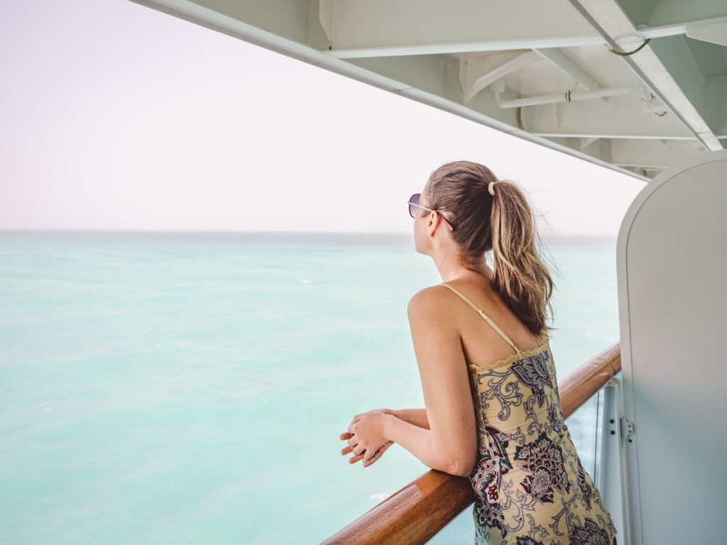 Woman enjoying ocean view from cruise ship balcony, highlighting holiday experiences booked through a cruise ship travel agent